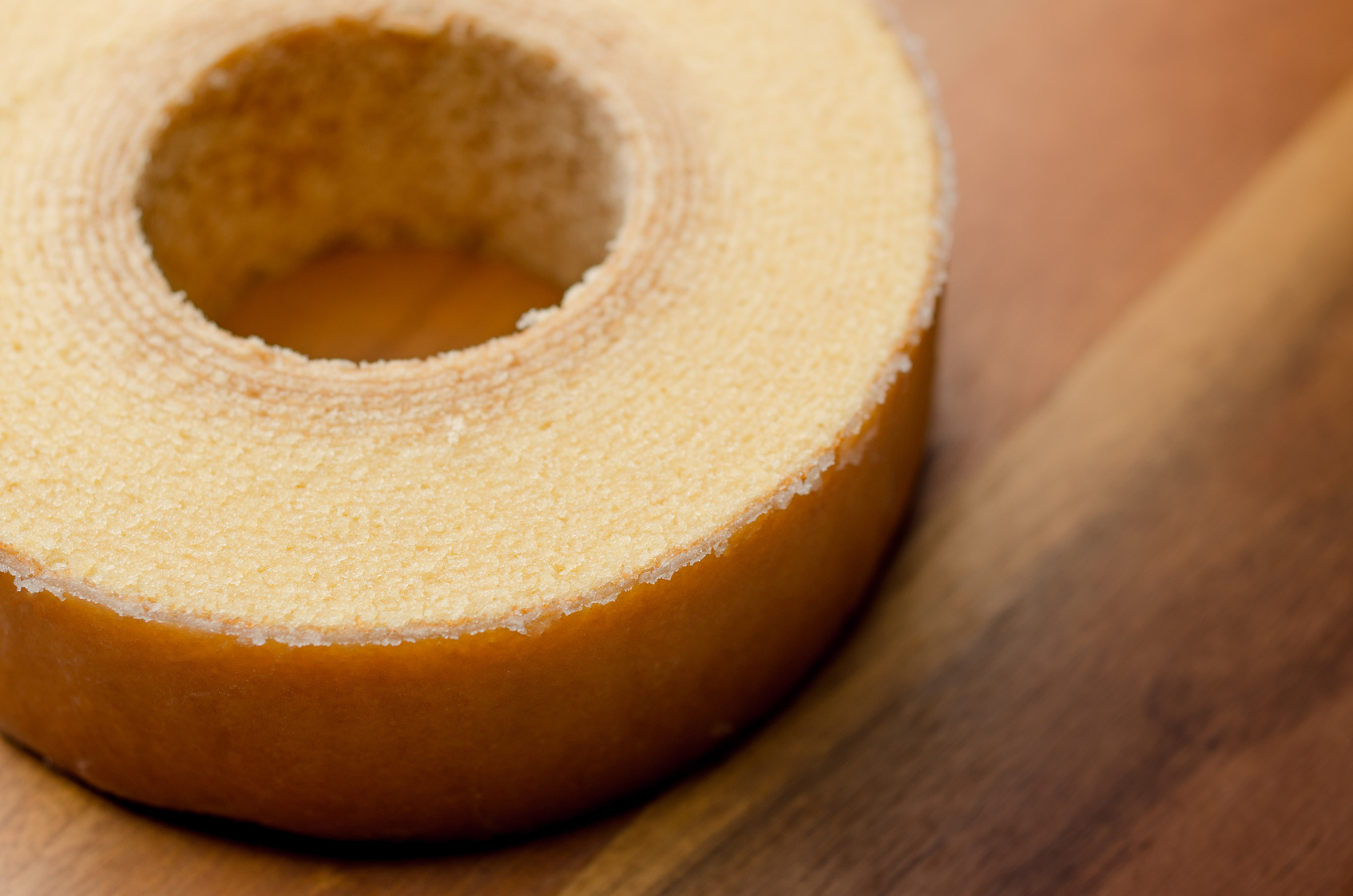 Close-up of a golden Bundt cake ring resting on a wooden surface, showing its crumbly texture and pale interior edge.