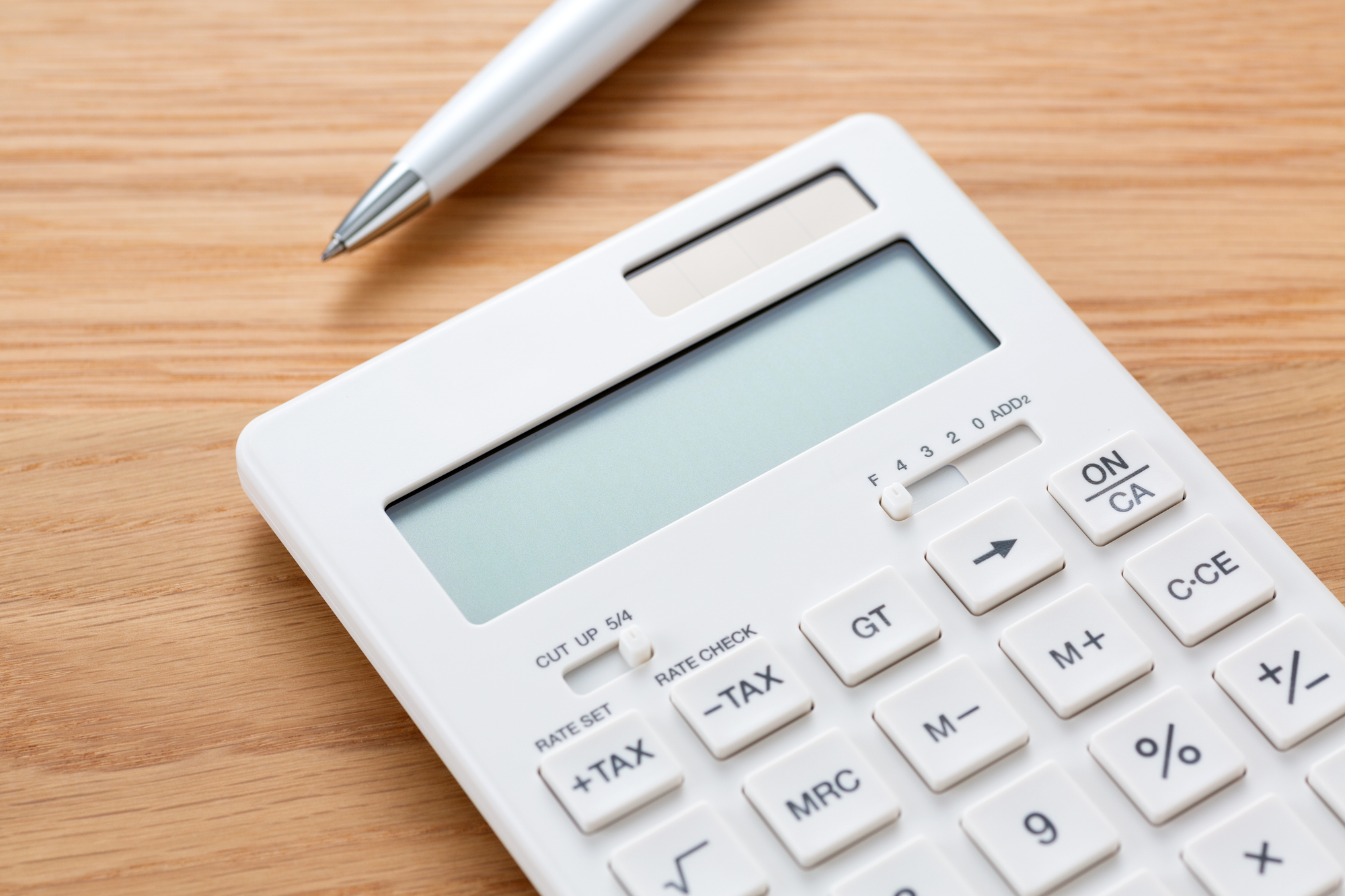 White calculator on a wooden desk with a silver pen beside it.