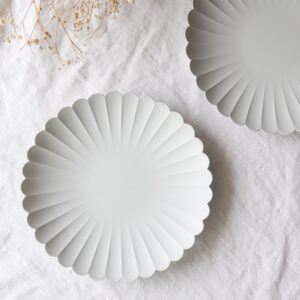 Decorative white paper fans arranged on white fabric with a sprig of dried baby's breath in the corner.