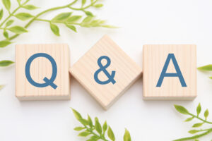 Wooden blocks spell 'Q & A' on a white background with green plant accents.